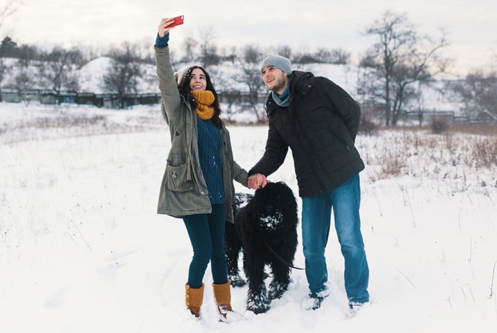 tutores tirando foto com cachorro preto na neva