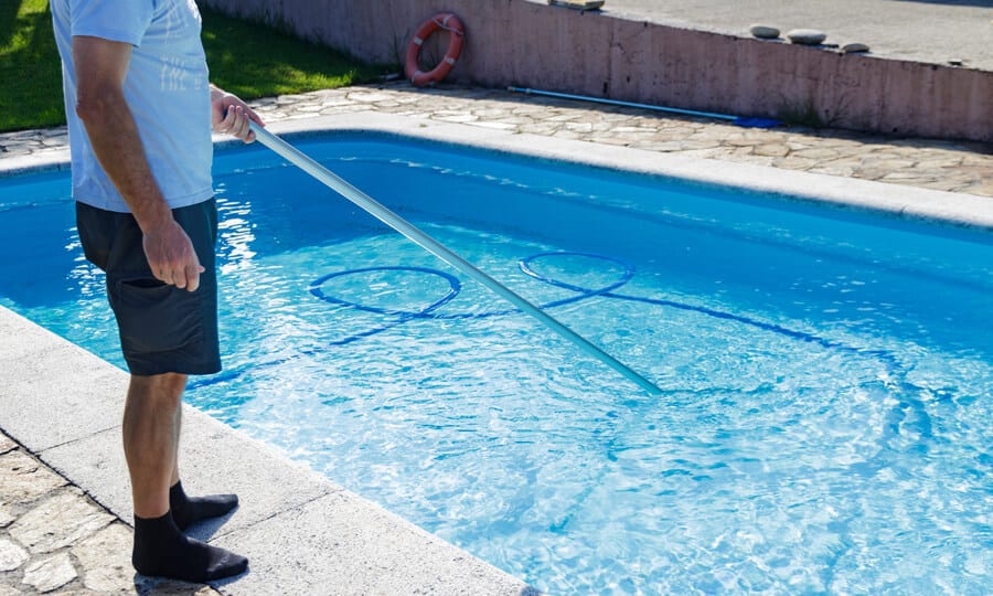 Homem limpando a piscina com azulejo azul claro.
