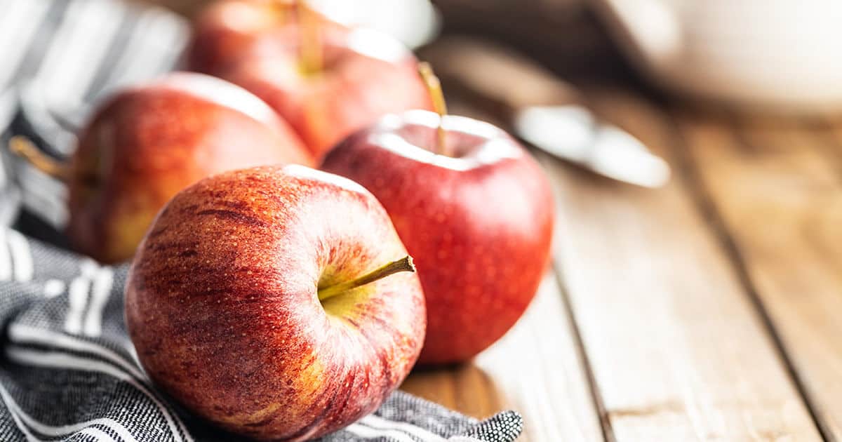 Quatro maçãs enfileiradas em cima da mesa de madeira.