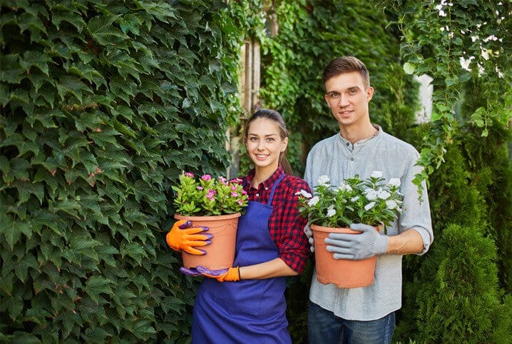 homeme e mulher segurando flores ao lado de plantas penduradas na parede