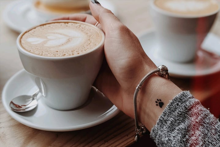 Mão com pulso tatuado segurando xícara de café