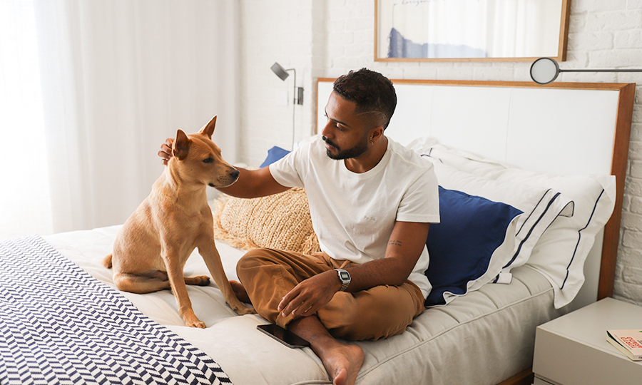 Homem sentado na cama com um cachorro.