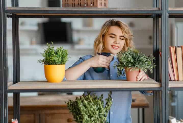 Mulher borrifando água em planta num vaso.