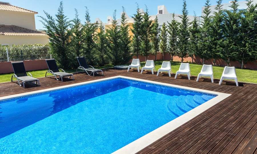 Piscina com deck de madeira e cadeiras brancas.