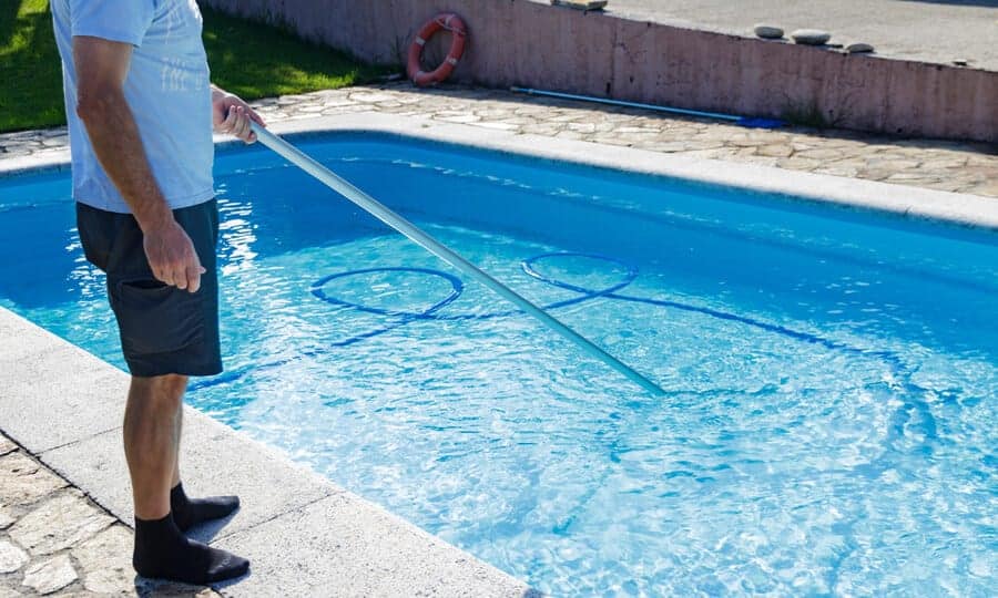 Como calcular o volume de água de uma piscina? Confira dicas 1 Homem limpando piscina.