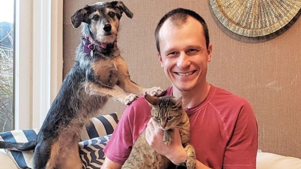 Dr. Pet segurando seu gato no colo e seu cachorro apoiando as patas em seu ombro.