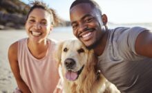 Homem e mulher sorrindo com o cachorro entre os dois.