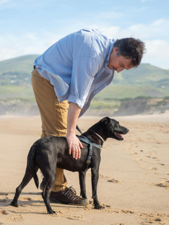 Responsável e cachorro de pelos pretos na praia.