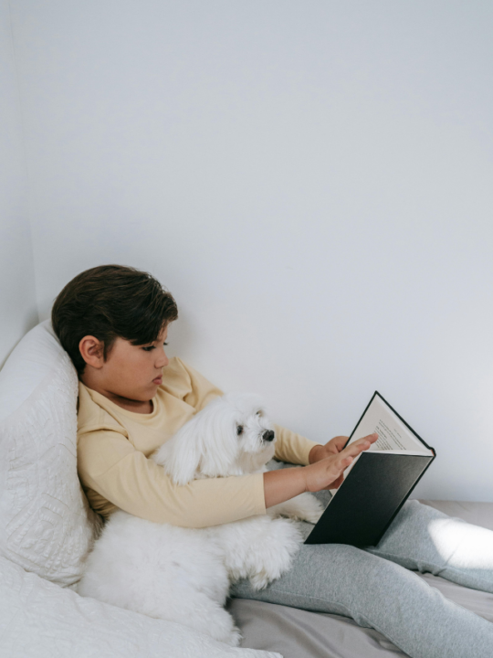 Menino lendo com seu cachorro ao lado.