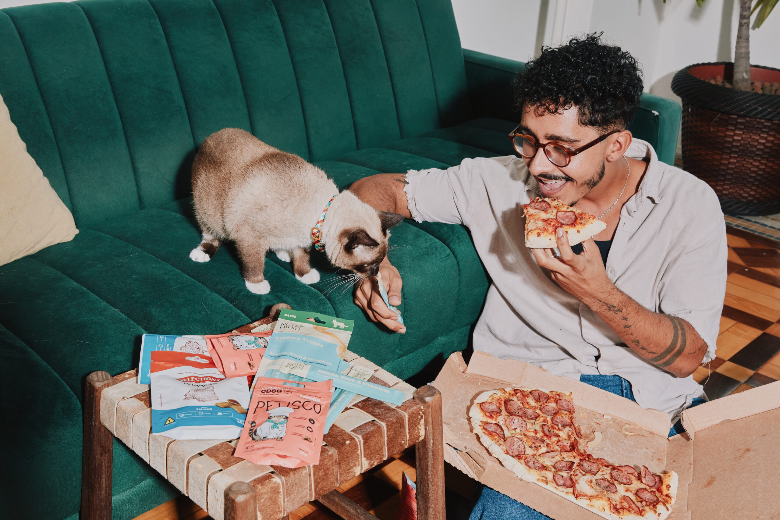 Tutor comendo pizza e oferecendo sachê para o gato com a outra mão.